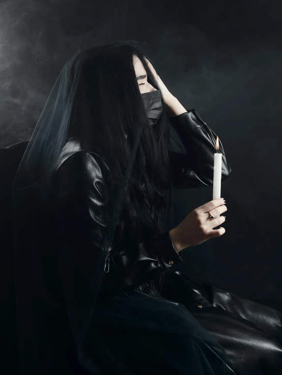 a woman sitting on a chair with a candle in her hand, an album cover, inspired by Nicola Samori, trending on pexels, gothic art, white man with black fabric mask, black haired girl wearing hoodie, smoking cigarette, jingna zhang