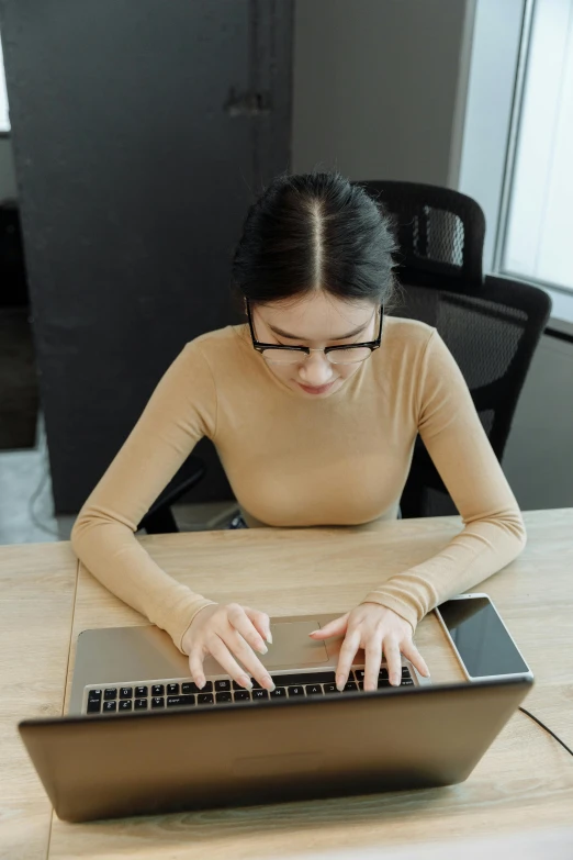 a woman sitting at a table using a laptop computer, wearing a cute top, asian features, 2019 trending photo, high angle