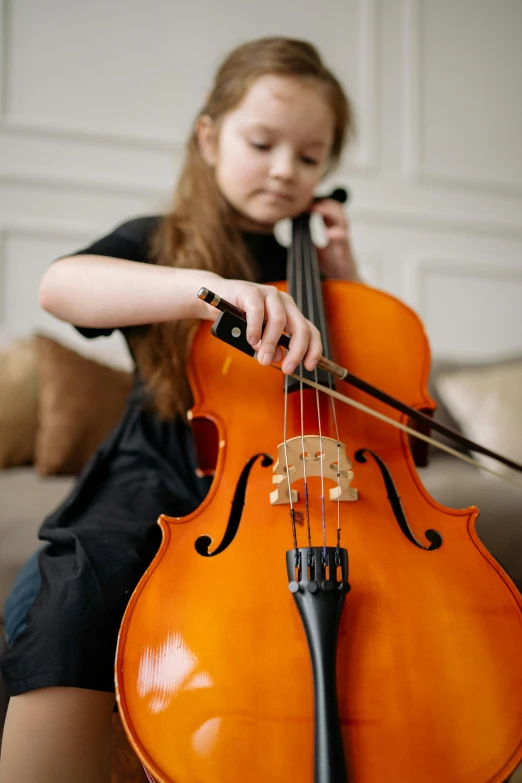 a young girl sitting on a couch playing a cello, pexels, avatar image, private school, high quality upload, small in size