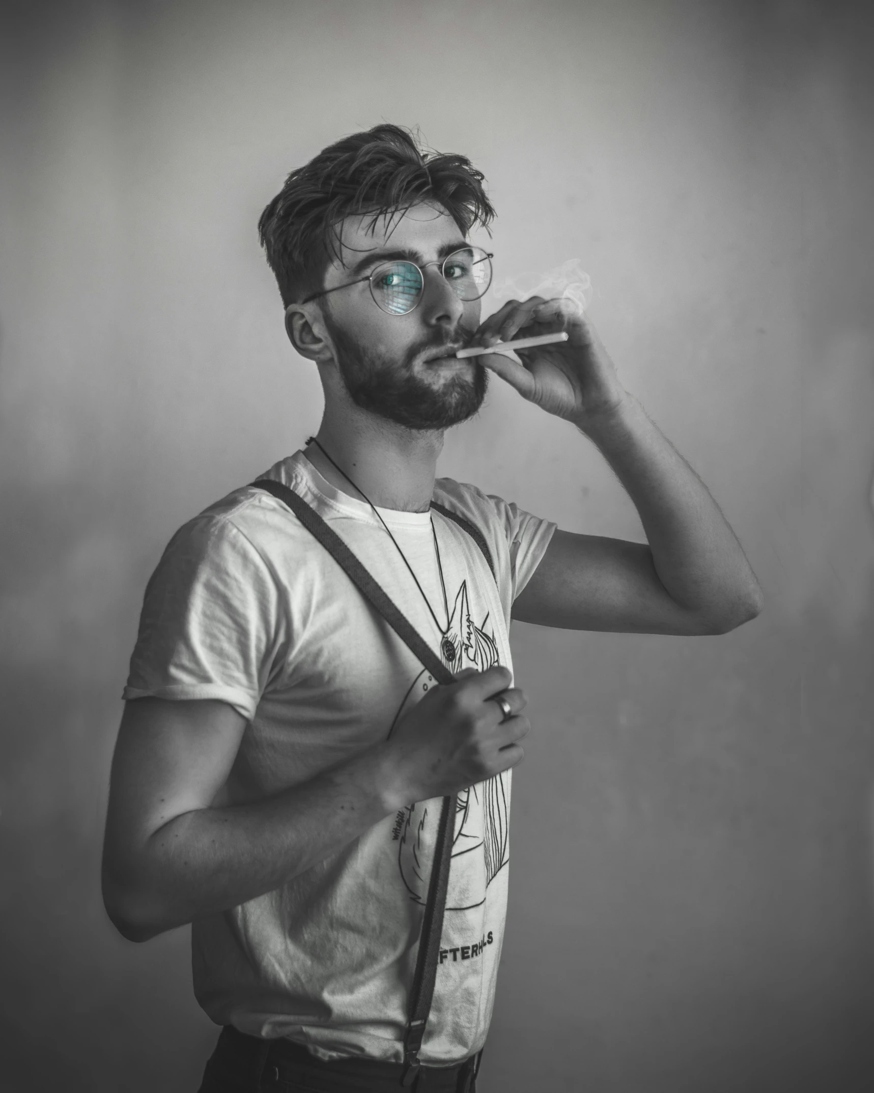 a black and white photo of a man smoking a cigarette, pexels contest winner, aestheticism, jewish young man with glasses, wearing a marijuana t - shirt, desaturated color, suspenders