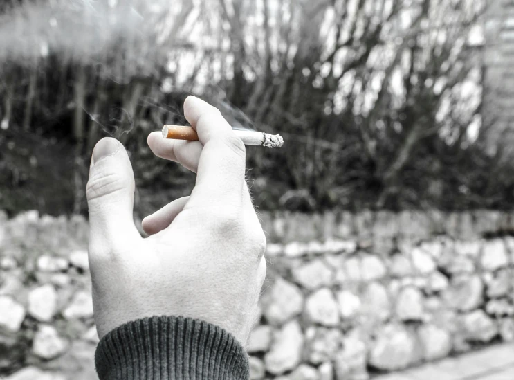 a person holding a cigarette in their hand, a black and white photo, by Kristian Zahrtmann, pexels, realism, selective color effect, high quality realistic, doing a thumb up, beautiful surroundings