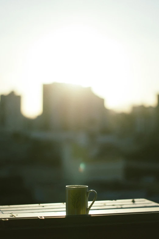 a coffee cup sitting on top of a wooden table, a picture, by Eizan Kikukawa, happening, city sunset, in sao paulo, is ((drinking a cup of tea)), cinestill 800t 50mm eastmancolor