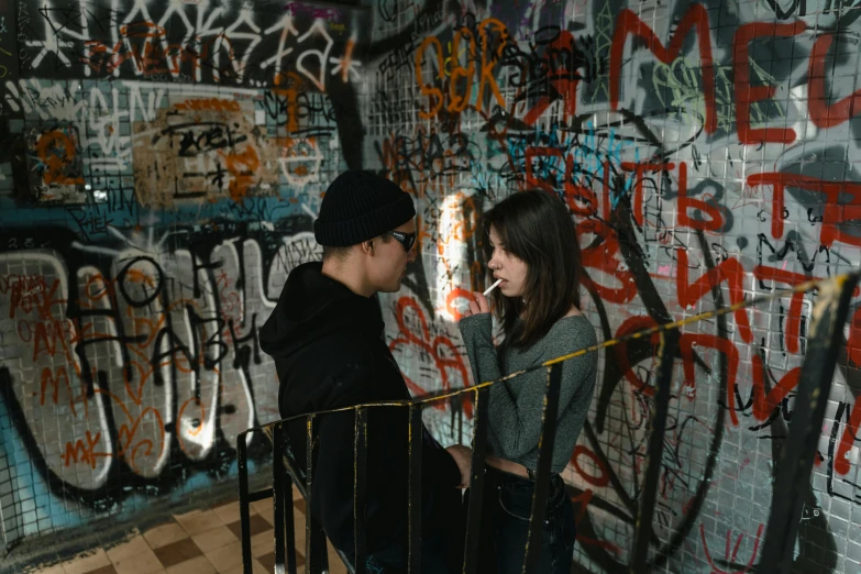 a man and a woman standing in front of a graffiti covered wall, a picture, by Elsa Bleda, pexels contest winner, graffiti, teenage girl, underground room, instagram picture, from a movie scene