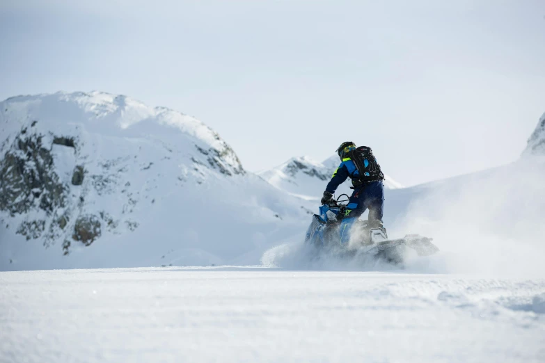 a man riding a snowmobile down a snow covered slope, by Haukur Halldórsson, pexels contest winner, epic mountains in the background, avatar image, 9 9 designs, blue