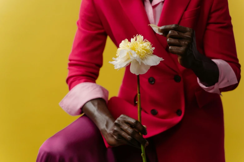 a woman sitting on a chair holding a flower, inspired by Ras Akyem, pexels contest winner, wearing a colorful men's suit, adut akech, mapplethorpe, pink and yellow