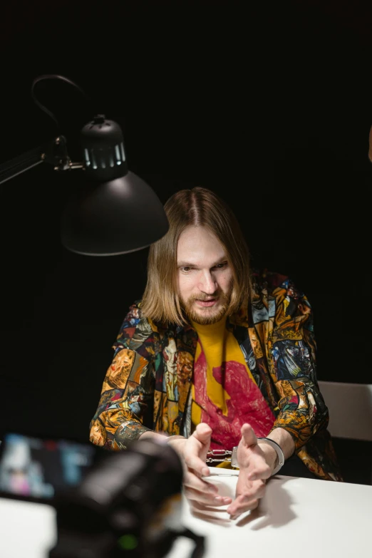 a man sitting at a table in front of a camera, an album cover, inspired by Daniël Mijtens, unsplash, looks like domhnall gleeson, in a photo studio, twitch streamer, alen kopera