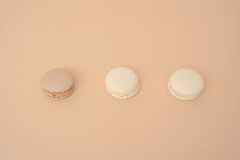 three macarons sitting next to each other on a pink surface, by Emma Andijewska, gradient brown to white, minimalist photo, ignant, sand color