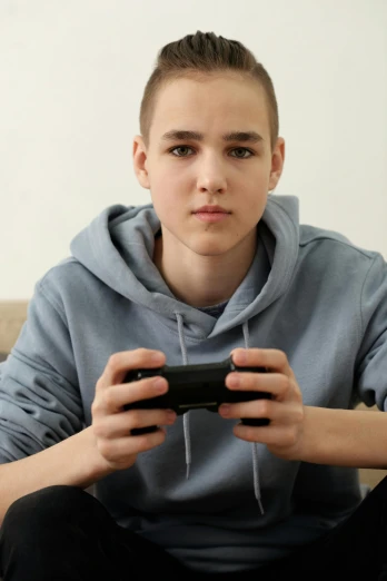 a young man sitting on a couch holding a video game controller, by artist, shutterstock, realism, buzz cut hair, 1 7 - year - old boy thin face, pouty, photograph taken in 2 0 2 0