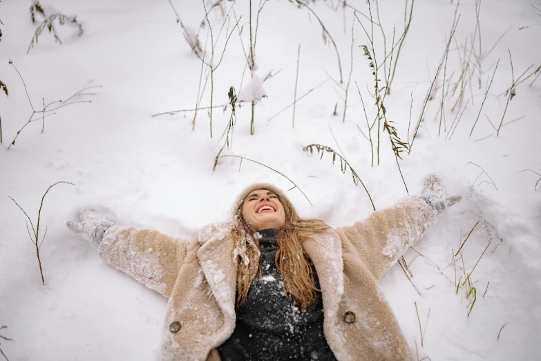 a woman laying in the snow with her arms outstretched, pexels contest winner, wearing hay coat, 🤬 🤮 💕 🎀, smiling down from above, blonde