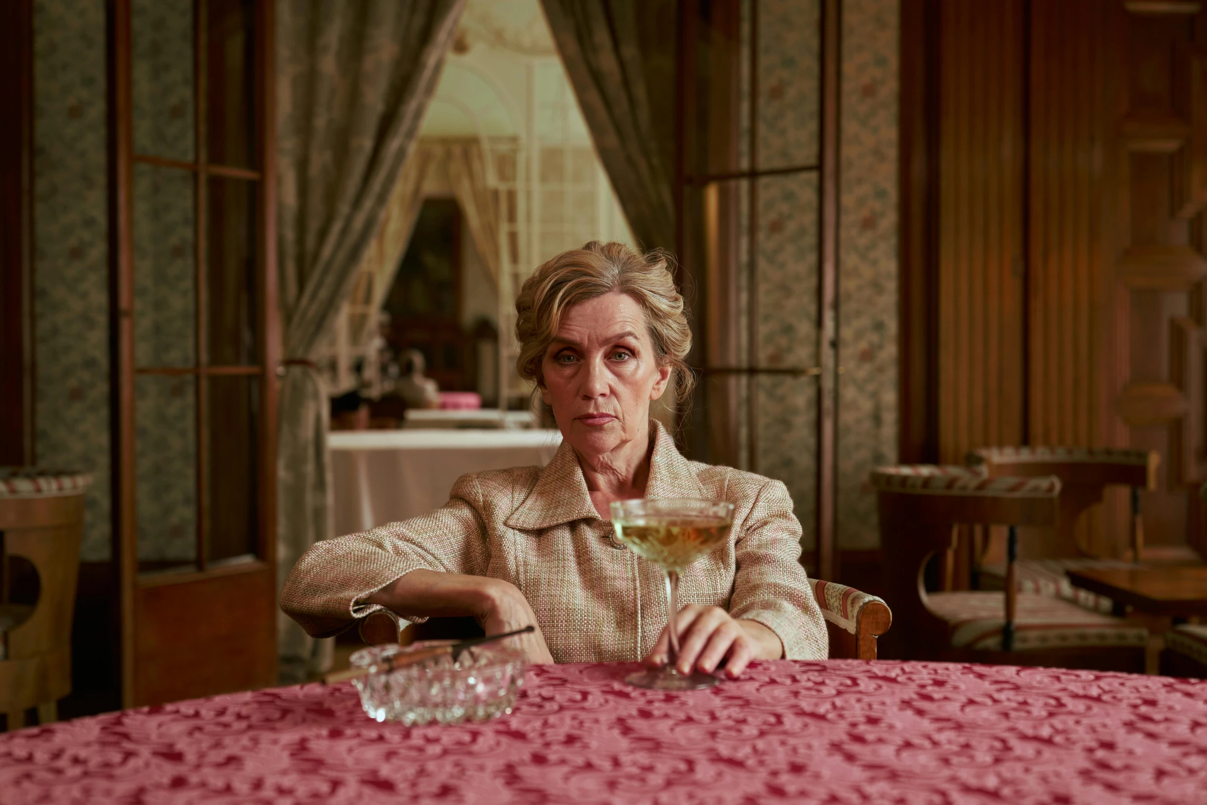 a woman sitting at a table with a glass of wine, a portrait, by Penelope Beaton, cinematic movie still, pink, square, anya forger