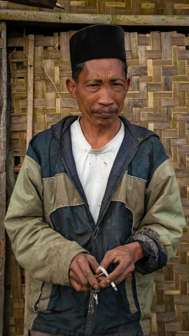 a man standing in front of a building holding a cigarette, a portrait, by Jan Tengnagel, sumatraism, bamboo, holds a small knife in hand, portrait image, farmer