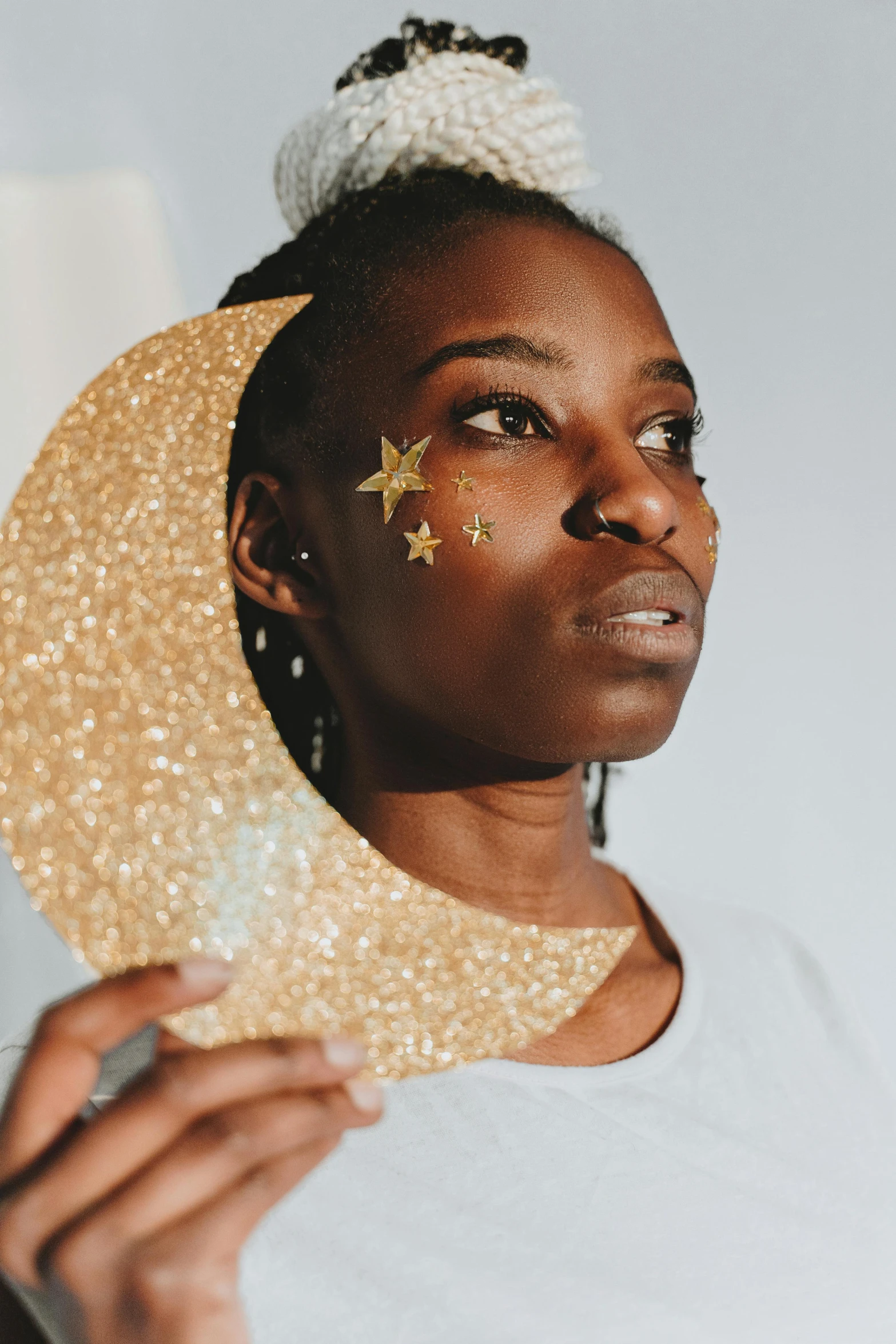 a close up of a person holding a hat, by Julia Pishtar, trending on pexels, afrofuturism, moon and stars, glitter sticker, gold decorations, young woman looking up