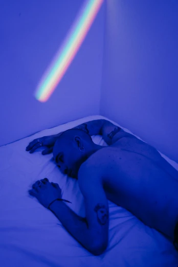 a man laying on top of a bed under a rainbow light, inspired by Elsa Bleda, holography, with blue skin, the last portrait of mac miller, muted rainbow tubing, out of body experience