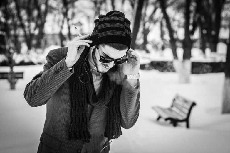 a man talking on a cell phone in the snow, a black and white photo, by Mathias Kollros, pexels, bauhaus, sunglasses and a scarf, at the park, dmitry prozorov style, wearing a tophat