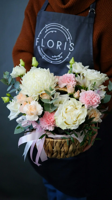 a woman in an apron holding a basket of flowers, a photo, inspired by Louis Hersent, light blush, on a dark background, carefully crafted, carnation