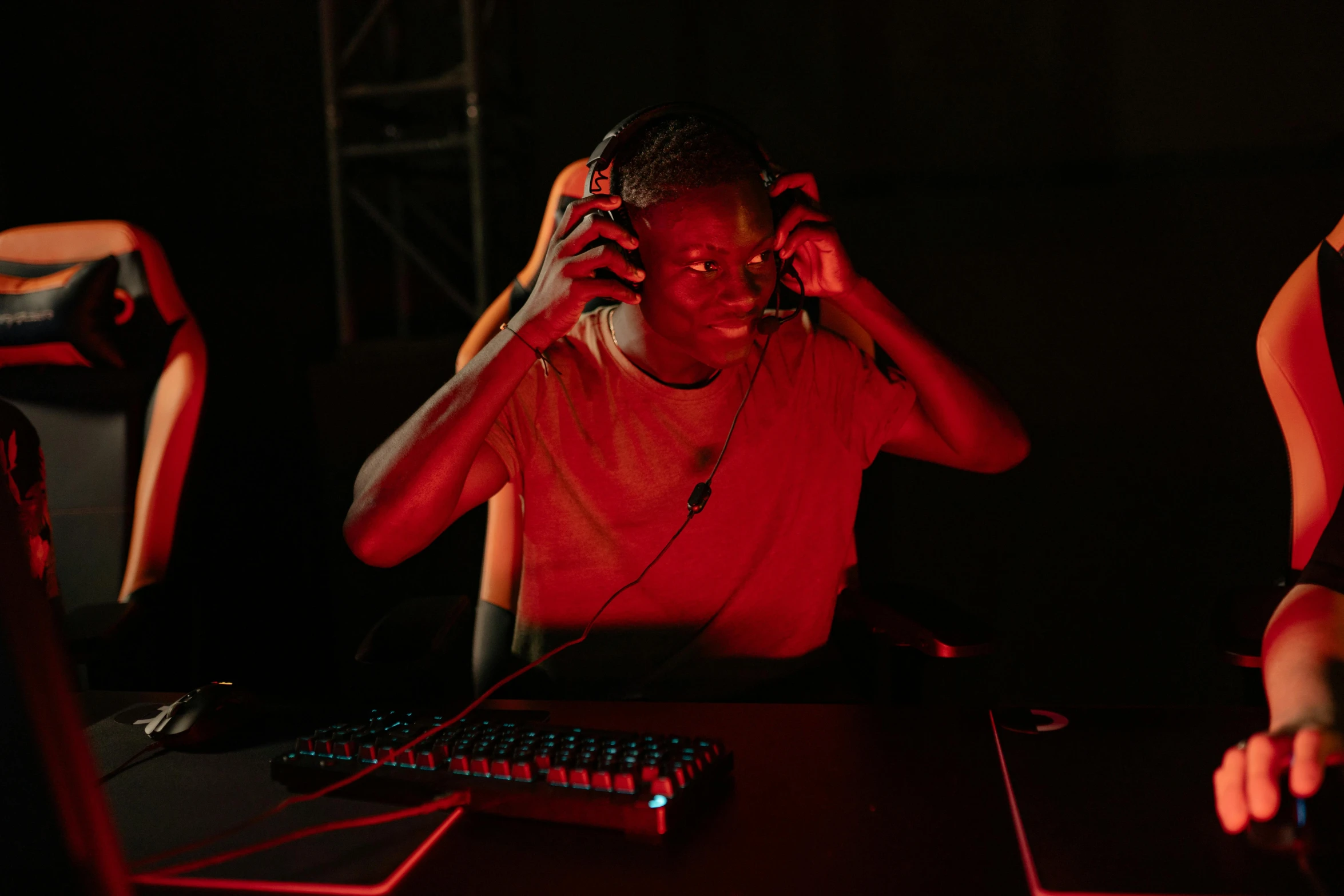 a man sitting at a desk in front of a computer, red aura, wearing gaming headset, ( ( dark skin ) ), game ready