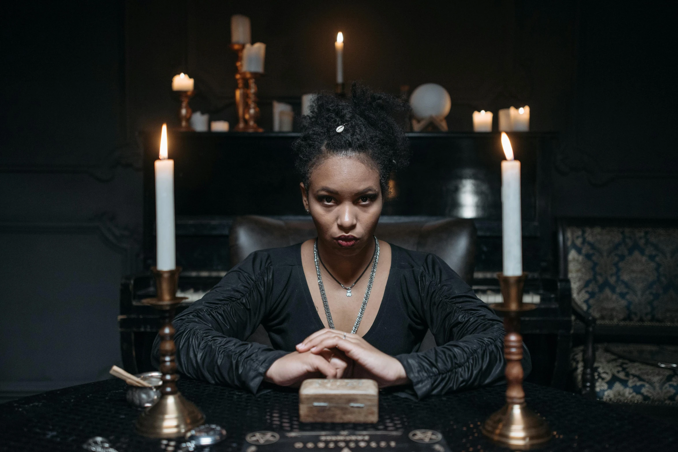 a woman sitting at a table with candles in front of her, a portrait, by Dan Frazier, pexels contest winner, occult robes, ashteroth, promotional image, black