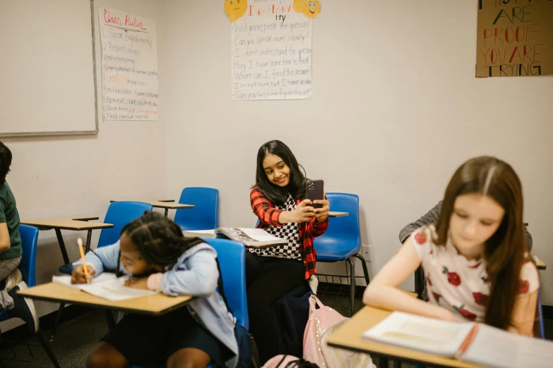 a group of children sitting at desks in a classroom, a portrait, by Carey Morris, trending on unsplash, goddess checking her phone, alexandria ocasio - cortez, woman holding another woman, ap news photograph