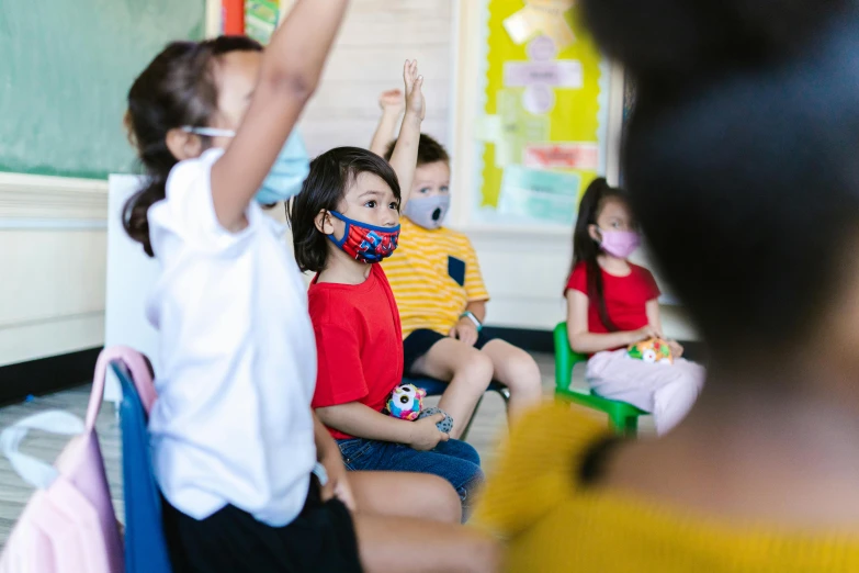 a group of children sitting on the floor with their hands in the air, by Nicolette Macnamara, pexels contest winner, ashcan school, surgical mask covering mouth, standing in class, haze over the shoulder shot, lachlan bailey