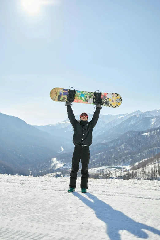 a man standing on top of a snow covered slope holding a snowboard, inspired by Tsuji Kakō, pexels contest winner, shin hanga, with arms up, russian and japanese mix, mountains at background, south korean male