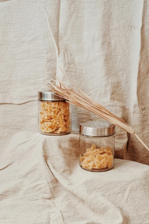 a couple of jars filled with food sitting on top of a table, a picture, unsplash, visual art, intricate pasta waves, textured base ; product photos, straw, stainless steel