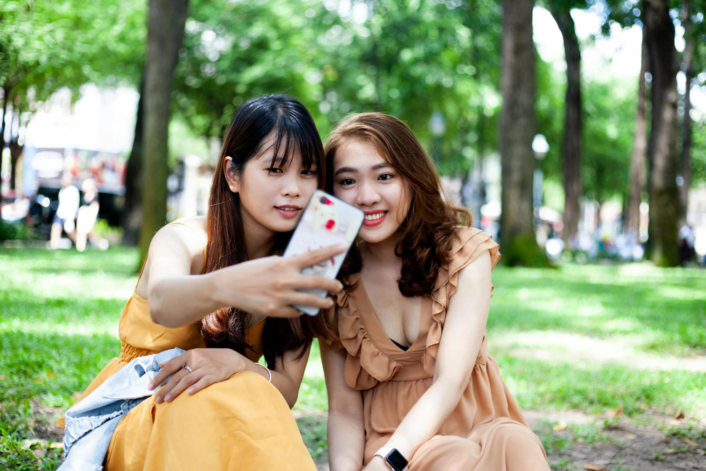 a couple of women sitting on top of a lush green field, a picture, shutterstock, realism, ao dai, 8k selfie photograph, square, in a city park