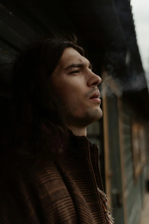 a man with long hair smoking a cigarette, an album cover, by Adam Dario Keel, trending on pexels, he is wearing a brown sweater, grainy footage, thoughtful )