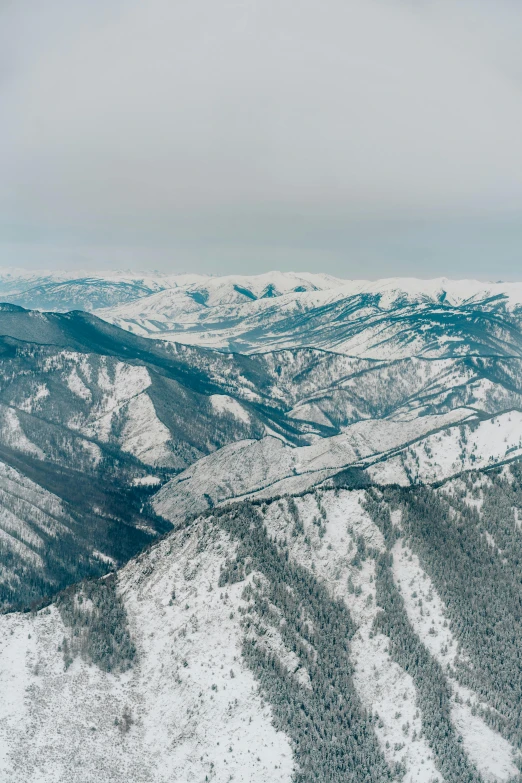 a man riding a snowboard on top of a snow covered slope, by Adam Marczyński, baroque, wide aerial shot, evergreen valley, seen from a plane, canyons