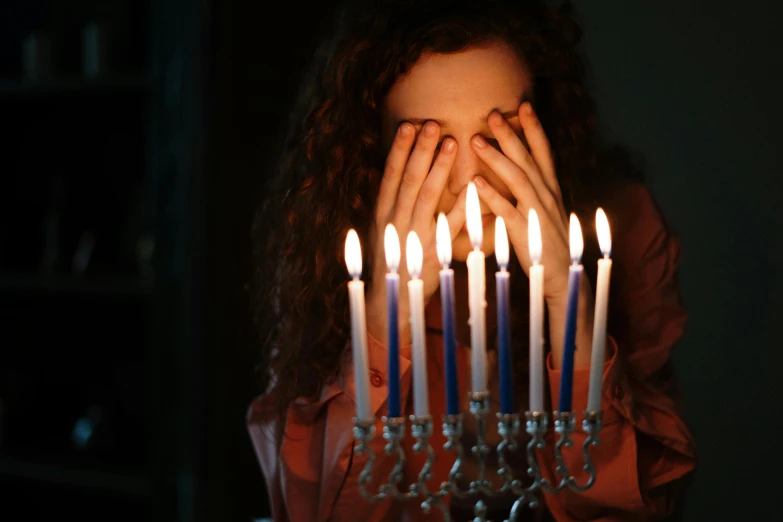 a woman holding a lit menorah in front of her face, pexels, teenager, dripping candles, instagram post, blind