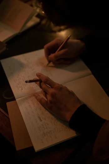 a person sitting at a table writing on a piece of paper, during the night, with some hand written letters, ignant, holding notebook