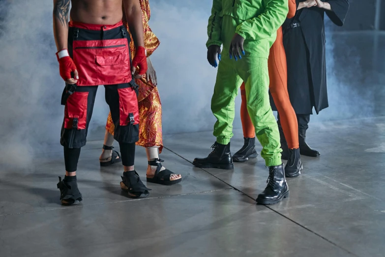 a group of people in costumes standing next to each other, by Nina Hamnett, trending on pexels, afrofuturism, futuristic balenciaga sneakers, stand on stone floor, wearing cargo pants, red and obsidian neon