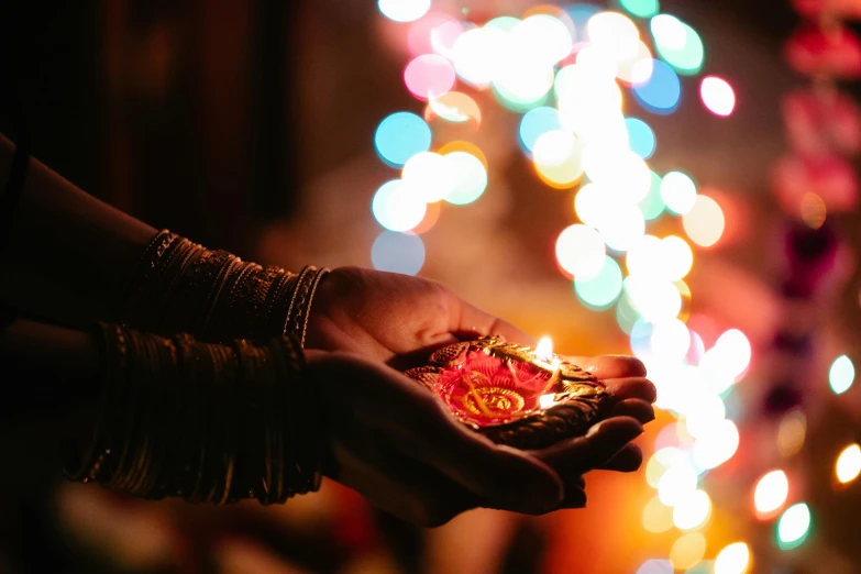 a close up of a person holding a small object, pexels contest winner, light and space, hindu ornaments, lots of lights, holiday vibe, a brightly coloured