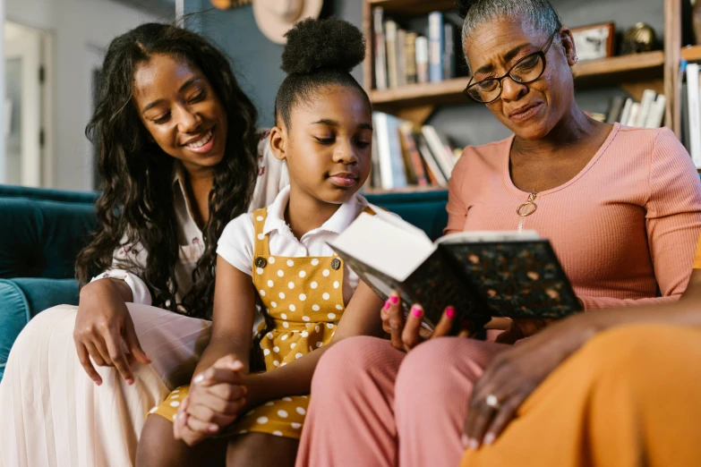 a woman and two girls sitting on a couch reading a book, by Carey Morris, pexels, black teenage girl, avatar image, maintenance photo, village girl reading a book