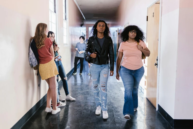 a group of people walking down a hallway, by Carey Morris, trending on pexels, happening, black teenage girl, lesbian, standing in class, wearing jeans