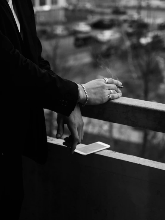 a man in a suit standing on a balcony, a black and white photo, by Niko Henrichon, unsplash, visual art, cigarette in hand, photo of a hand jewellery model, phone in hand, holding a wood piece