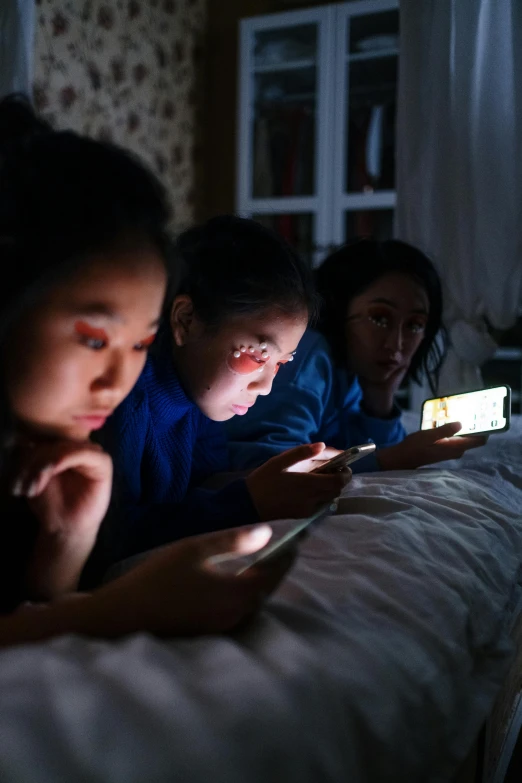 a group of children laying on a bed looking at a cell phone, inspired by Zhang Xiaogang, pexels, at twilight, asian women, nightlight, slide show