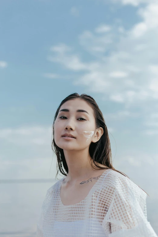 a woman standing on top of a beach next to the ocean, inspired by Ai Xuan, trending on pexels, hyperrealism, beauty mark on cheek, gemma chan girl portrait, ethnicity : japanese, on clouds