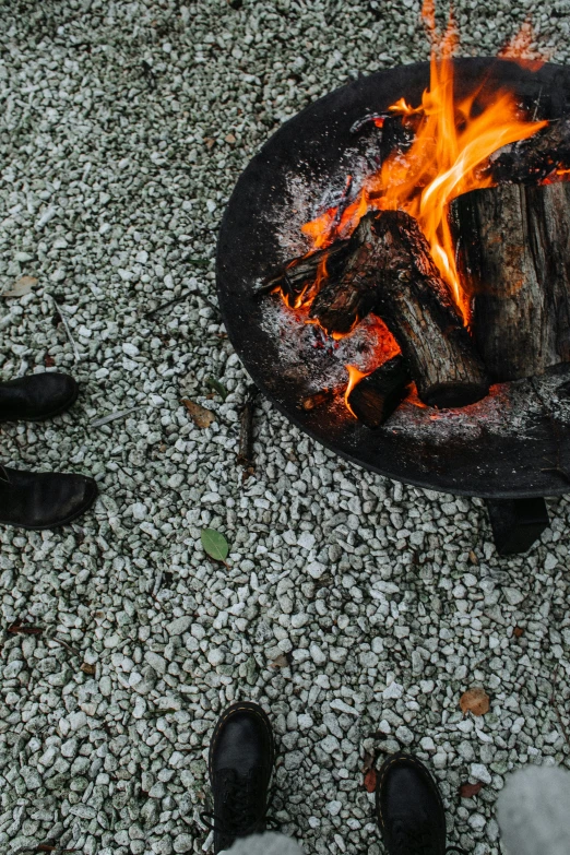 a group of people standing around a campfire, by Elsa Bleda, visual art, cow hoof feet, gravel, black main color, grey