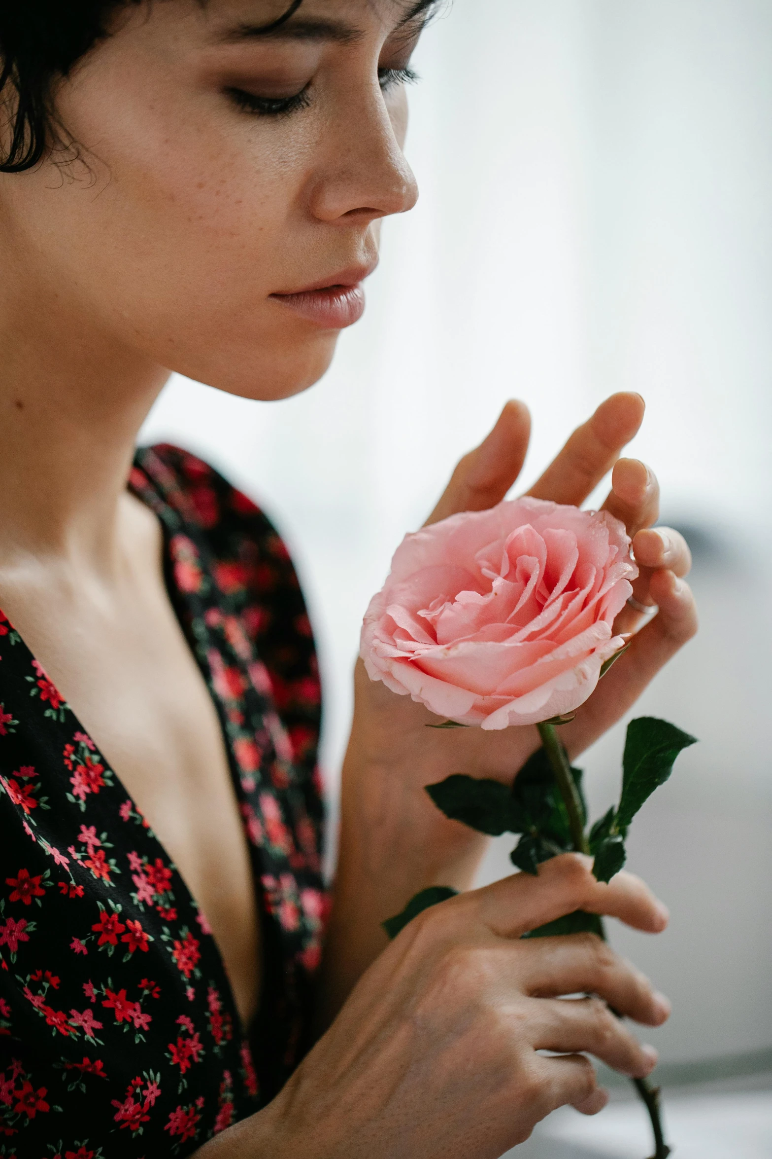 a woman holding a pink rose in her hand, inspired by Elsa Bleda, trending on pexels, romanticism, looking off to the side, decolletage, wearing a velvet robe, femalev beauty