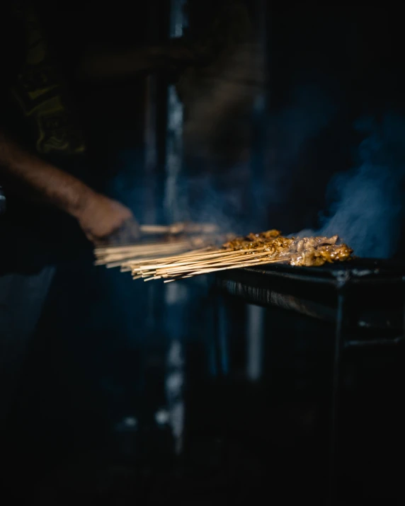 a person cooking food on a grill in the dark, holding a wooden staff, profile image, multiple stories, malaysian