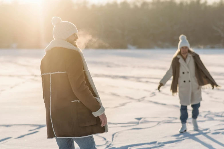 a couple of people walking across a snow covered field, by Eero Järnefelt, trending on pexels, warm sunshine, brown, woman, winter lake setting