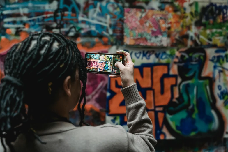 a woman taking a picture of a graffiti wall, trending on pexels, avatar image, iphone video, vhs colour photography, black graffiti