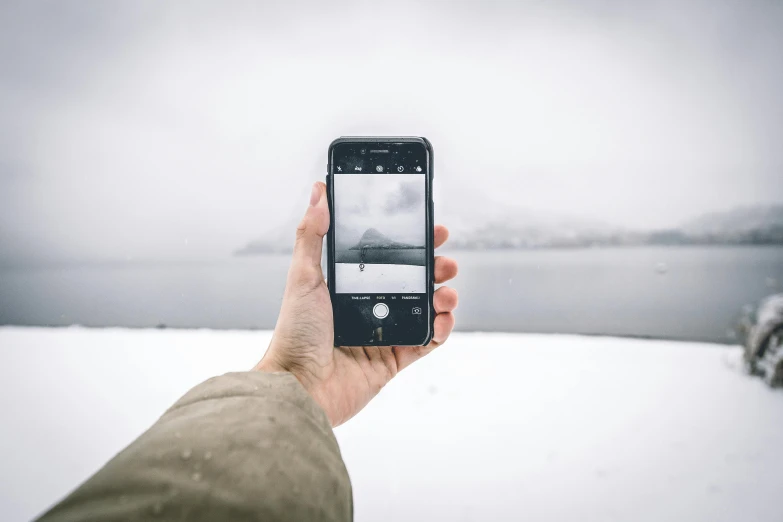 a person taking a picture of a lake in the snow, mobile learning app prototype, looking directly at the viewer, minimalistic, iphone