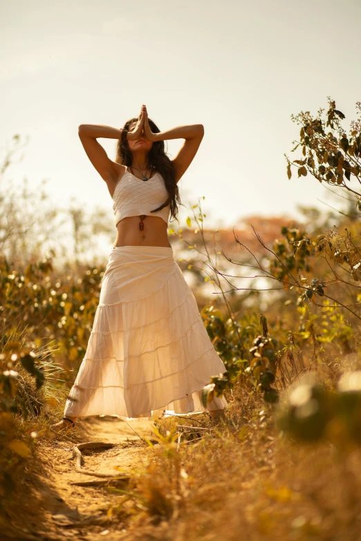 a woman standing in a field with her hands behind her head, wearing white skirt, prana, beautifully lit, magali