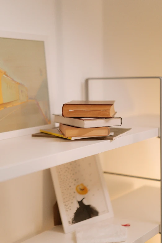 a lamp sitting on top of a white shelf next to a painting, a picture, stack of books on side table, zoomed in, studio product shot, yellow lighting from right
