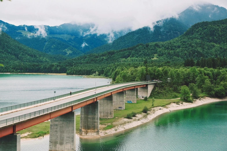 a bridge over a body of water with mountains in the background, an album cover, inspired by Thomas Struth, unsplash contest winner, hurufiyya, austrian architecture, highways, 🚿🗝📝, still from a wes anderson movie