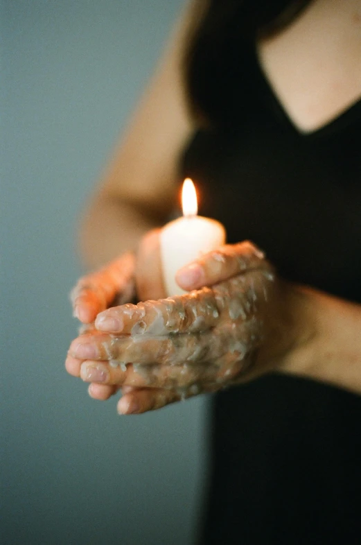 a woman holding a lit candle in her hands, pexels, made of wax and water, instagram post, battered, foam