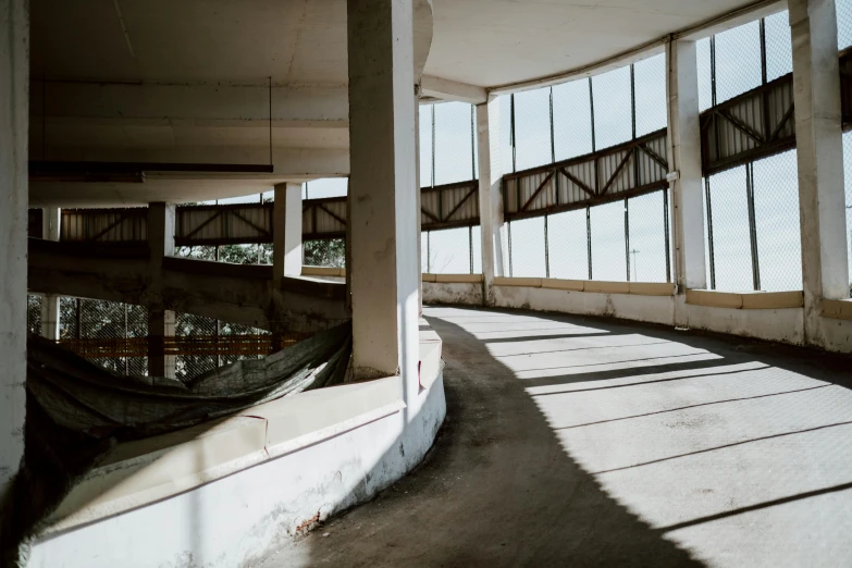 a man riding a skateboard up the side of a ramp, by Lee Loughridge, unsplash contest winner, brutalism, 70s interior with arched windows, decaying dappled sunlight, observation deck, standing in a large empty hall