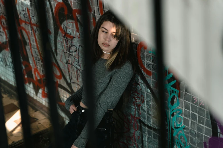 a woman leaning against a wall with graffiti on it, inspired by Elsa Bleda, pexels contest winner, portrait of depressed teen, stood in a cell, mid 2 0's female, girl with brown hair