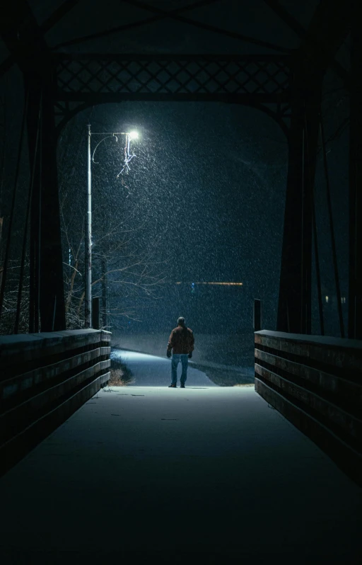 a man walking across a bridge at night, poster art, inspired by Gregory Crewdson, pexels contest winner, light snowfall, 8k cinematic lighting, wyoming, single portrait